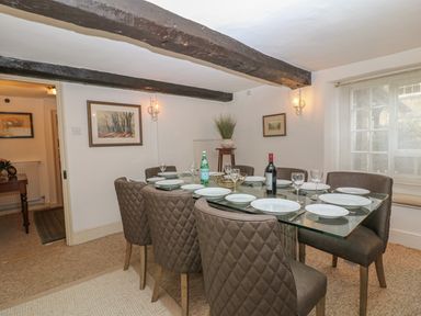 A dining room with a glass table set with plates and glasses eight chairs and exposed wooden ceiling beams at Dolphin House in Burford