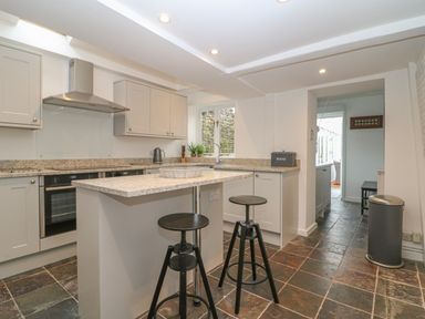 A kitchen with a central island and two stools a bread bin and a trash can on a tiled floor at Dolphin House in Burford