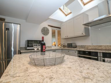 A kitchen with a metal fruit basket on a countertop wine bottle and glasses near a microwave and a stainless steel refrigerator at Dolphin House in Burford