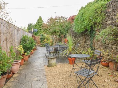 A garden patio with two metal tables and chairs surrounded by potted plants and stone walls at Dolphin House in Burford