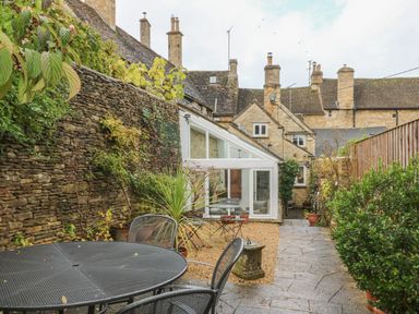 A garden with a stone wall metal table and chairs potted plants and a glass extension at Dolphin House in Burford