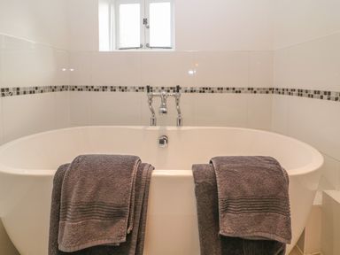 A bathroom with a white freestanding bathtub and two gray towels hanging on the edge at Dolphin House in Burford
