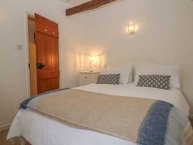 A bedroom with a double bed two pillows a nightstand lamp wooden door and a wall light at Dolphin House in Burford