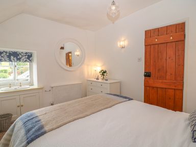 A bedroom with a bed a wooden door a white dresser a round mirror and a window with blue patterned blinds at Dolphin House in Burford