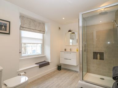 A bathroom with a toilet a window with blinds a wall-mounted sink unit with mirror and lights and a glass-enclosed shower at Dolphin House in Burford