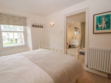 A bedroom with a white metal bed frame a window with floral blinds and an open door leading to a bathroom at Dolphin House in Burford