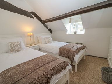 A bedroom with two single beds a nightstand with a lamp a window a chest of drawers and exposed wooden beams at Dolphin House in Burford