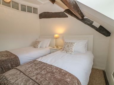 A bedroom with two single beds a bedside table and lamp under exposed wooden beams at Dolphin House Burford