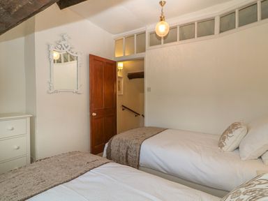 A bedroom with two single beds a white dresser a wooden door and a decorative wall mirror at Dolphin House in Burford
