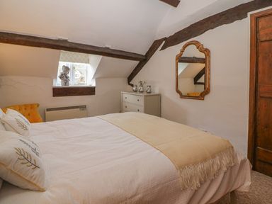 A bedroom with a bed a yellow chair a window with a bust on the sill a mirror on the wall and a white chest of drawers at Dolphin House in Burford