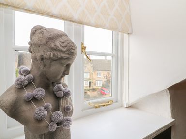 A stone bust with a decorative pom pom necklace on a windowsill with a window showing buildings outside at Dolphin House in Burford