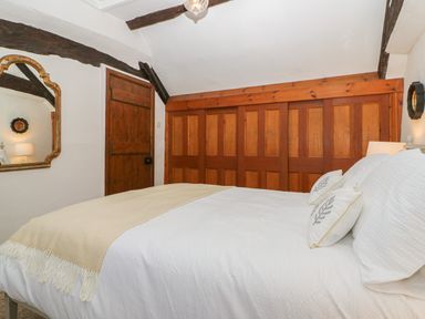 A bedroom with a bed covered in white bedding and pillows next to a wooden wardrobe and door at Dolphin House in Burford