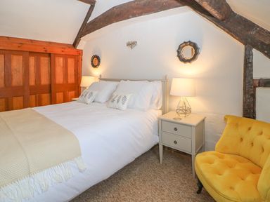 A bedroom with a double bed two bedside tables with lamps a yellow chair and wooden beams on the ceiling at Dolphin House in Burford