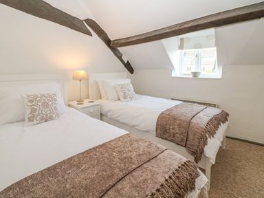 A bedroom with two single beds a lamp on a bedside table and a window at Dolphin House in Burford