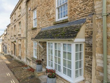 Stone exterior of a building with white framed windows and planting pots on a narrow street at Dolphin House in Burford