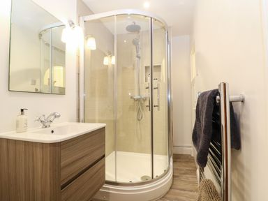 A bathroom with a wooden vanity sink unit a glass enclosed corner shower and a chrome towel radiator at Dolphin House in Burford