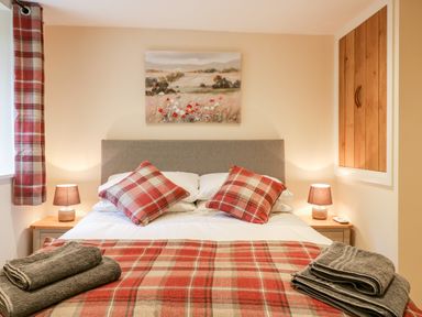 A bedroom with a double bed two bedside tables with lamps folded towels and plaid cushions at Tillys Cottage in Edington