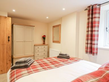 A bedroom with a bed covered in plaid fabric towels on the bed and matching curtains at Tilly's Cottage in Edington