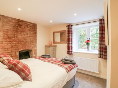 A bedroom with a bed pillows chest of drawers and window with red plaid curtains and flowers at Tilly's Cottage in Edington