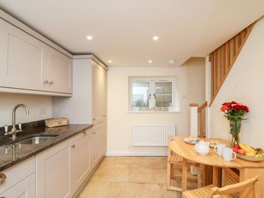 A kitchen with beige cabinets a granite countertop a wooden table with chairs and a vase of flowers at Tilly's Cottage in Edington
