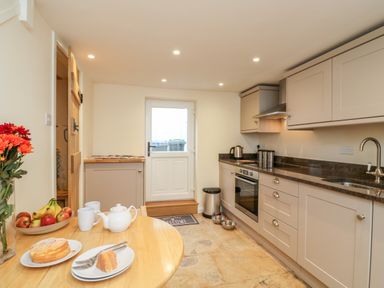 A kitchen with beige cabinets a wooden table with cake flowers and fruit at Tillys Cottage in Edington