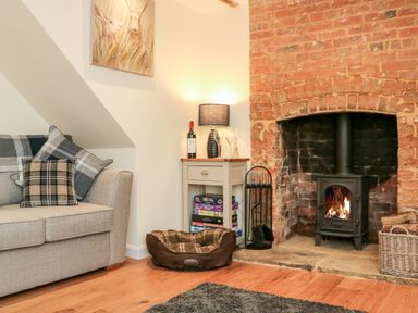A living room with a sofa pillows small table wine lamp fireplace and dog bed at Tilly's Cottage in Edington