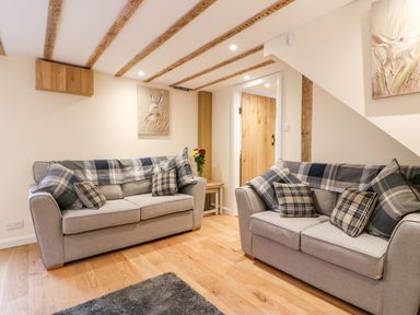 A living room with two gray sofas with plaid blankets and pillows a wooden floor and a small wooden table with flowers at Tilly's Cottage in Edington