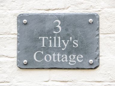 A stone house number plaque with the text 3 Tilly's Cottage on a white brick wall at Tilly's Cottage in Edington