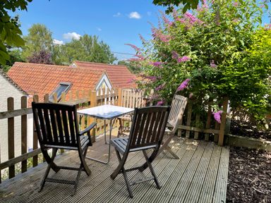 A wooden deck with four chairs and a small table next to a wooden fence and flowering bush at Tillys Cottage in Edington