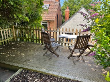 A wooden deck with three wooden chairs and a small table surrounded by a wooden fence and plants at Tillys Cottage in Edington