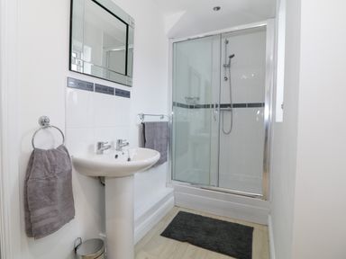 A bathroom with a pedestal sink, mirror, shower enclosure with sliding glass doors, towels, and a black bath mat at 8 Marina View in Pwllheli