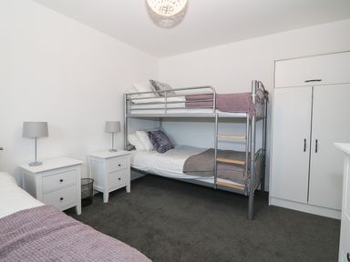 A bedroom with bunk beds a single bed two bedside tables with lamps and a wardrobe at 8 Marina View in Pwllheli