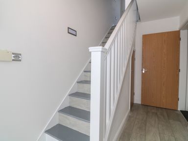 A staircase with wooden steps and white railing next to a wooden door in a hallway at 8 Marina View in Pwllheli