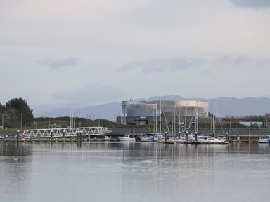 A marina with boats docked near a modern industrial building and mountains in the background at 8 Marina View in Pwllheli
