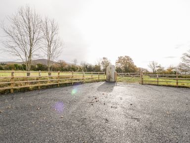 An asphalt driveway with wooden fences and a stone pillar near a wooden gate at Rhydau Cottage in Pentir near Deiniolen