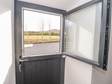 An open stable door with a window showing a fenced grassy field and trees at Rhydau Cottage in Pentir near Deiniolen