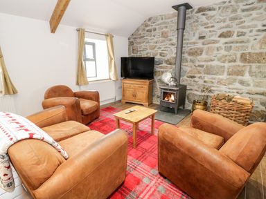 A living room with brown armchairs a wood burning stove a television and a red plaid carpet at Rhydau Cottage in Pentir near Deiniolen