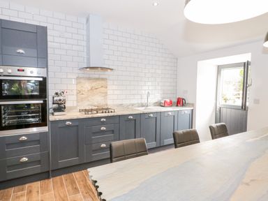 A kitchen with dark cabinets a marble countertop tiled backsplash and wooden floor at Rhydau Cottage in Pentir near Deiniolen