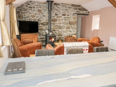 A living room with a stone wall wood burning stove television brown armchairs and a light blue table at Rhydau Cottage in Pentir near Deiniolen