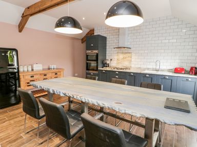 A kitchen with a large wooden table surrounded by six black chairs under two black pendant lights at Rhydau Cottage in Pentir near Deiniolen