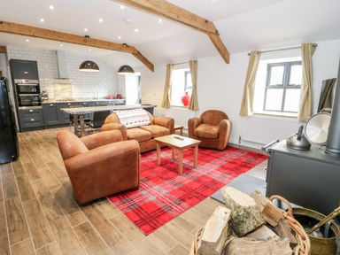 An open plan living room and kitchen with brown armchairs and sofa on a red patterned rug at Rhydau Cottage in Pentir near Deiniolen