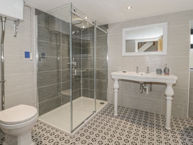 A bathroom with a glass shower enclosure a toilet a sink with two taps and a mirror at Rhydau Cottage in Pentir near Deiniolen