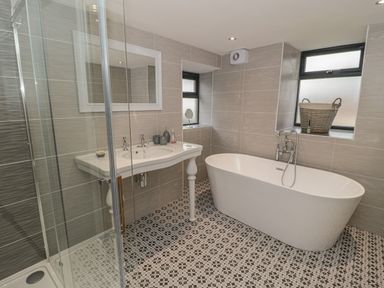 A bathroom with a freestanding bathtub a sink with two taps a large mirror a glass shower enclosure and patterned floor tiles at Rhydau Cottage in Pentir near Deiniolen