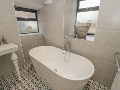 A bathroom with a freestanding bathtub a sink with toiletries two windows and a basket on the windowsill at Rhydau Cottage Pentir near Deiniolen