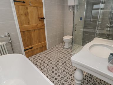 A bathroom with a wooden door a toilet a shower cubicle a white bathtub and a white sink unit with patterned floor tiles at Rhydau Cottage in Pentir near Deiniolen