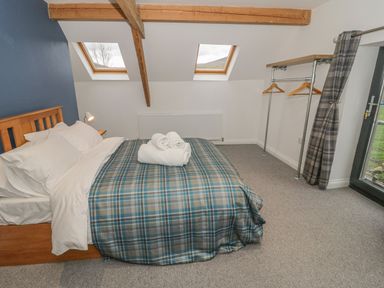 A bedroom with a wooden bed a blue plaid bedspread rolled white towels two skylights an open clothes rack and a glass door at Rhydau Cottage in Pentir near Deiniolen