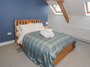 A bedroom with a wooden bed a plaid bedspread rolled towels on the bed a bedside table with a lamp and skylight windows at Rhydau Cottage in Pentir near Deiniolen