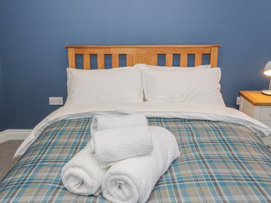 A bed with white pillows and towels on a plaid bedspread in a bedroom at Rhydau Cottage in Pentir near Deiniolen
