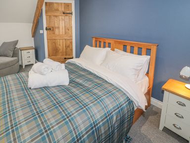 A bedroom with a wooden bed frame and plaid bedding with white towels on the bed at Rhydau Cottage in Pentir near Deiniolen