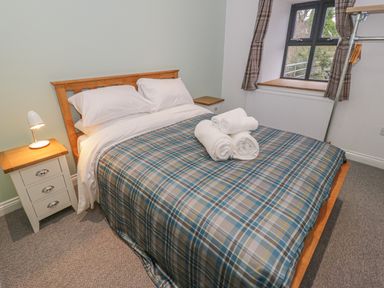 A bedroom with a double bed with plaid bedding rolled towels bedside tables a window and a lamp at Rhydau Cottage in Pentir near Deiniolen